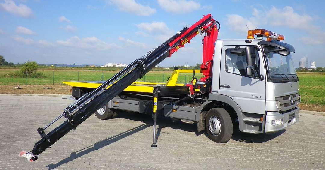 Mercedes crane truck with its boom extended, parked on paving.